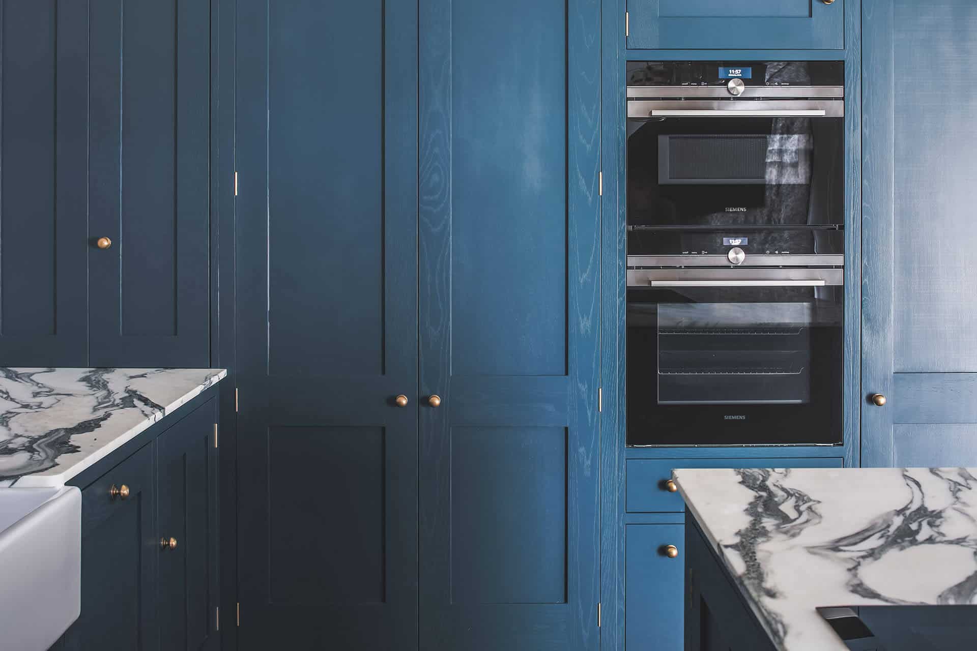 Dark blue geometric kitchen with larder cabinet and integrated eye level ovens