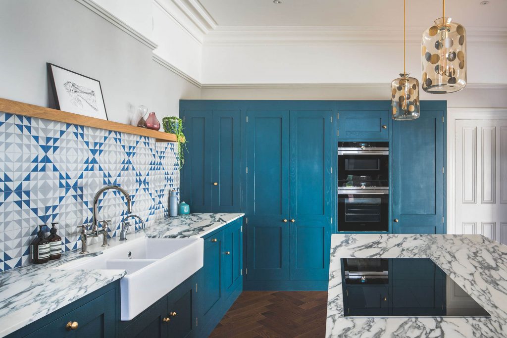 Dark blue geometric kitchen with tall cabinets, integrated ovens and marble worktop