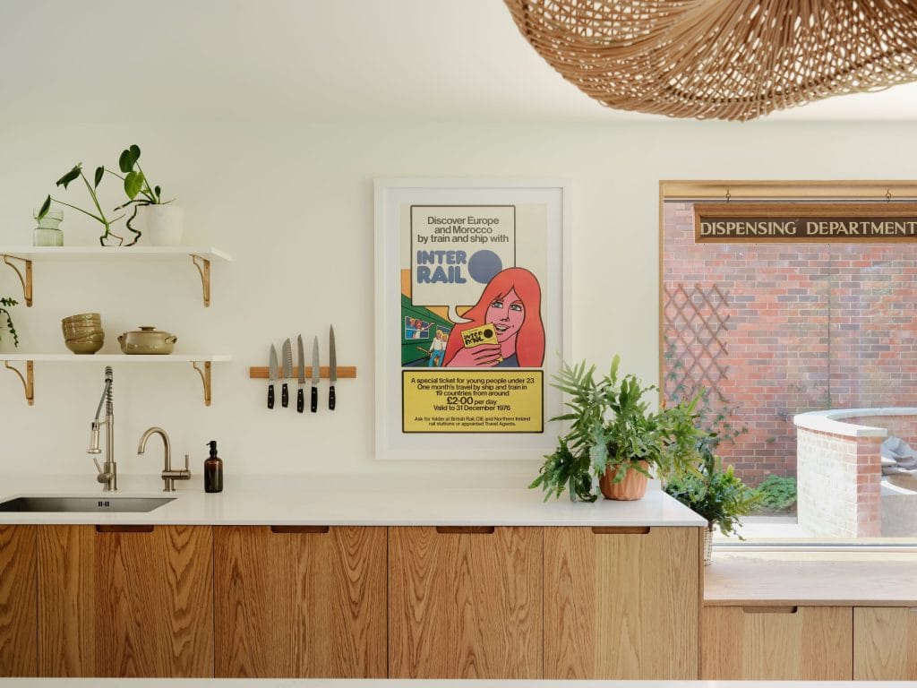 Wide shot of a modern, contemporary kitchen. White walls with accents of green plants in terracotta pots. There is a set of oak-veneered cabinets, with integrated scoop handles. A Caesarstone Calacatta Nuvo polished worktop sits on top of the cabinets. It's a warm and inviting space - designed for the family.