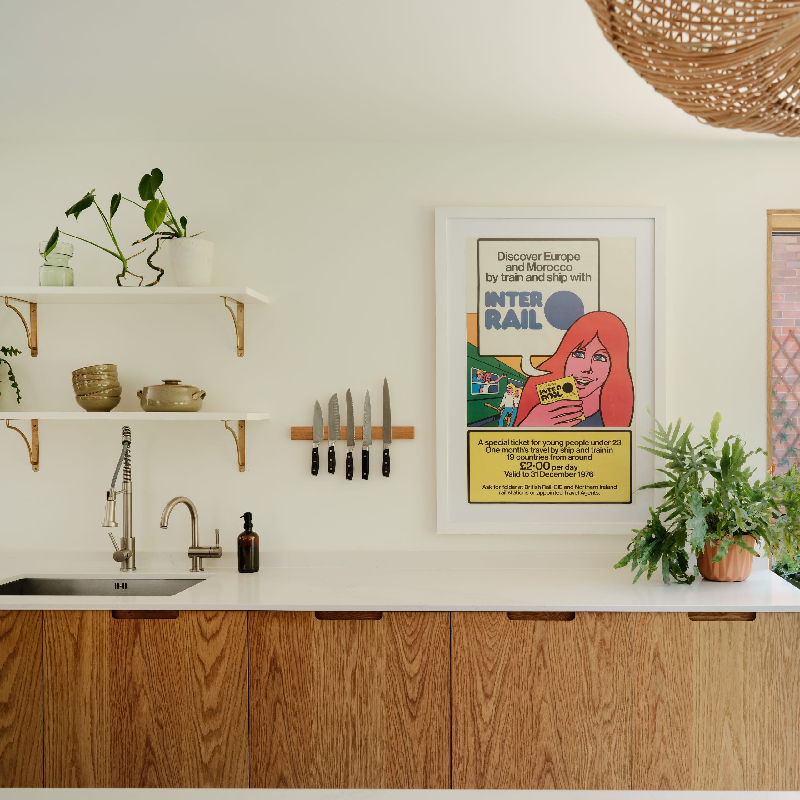 Wide shot of a modern, contemporary kitchen. White walls with accents of green plants in terracotta pots. There is a set of oak-veneered cabinets, with integrated scoop handles. A Caesarstone Calacatta Nuvo polished worktop sits on top of the cabinets. It's a warm and inviting space - designed for the family.