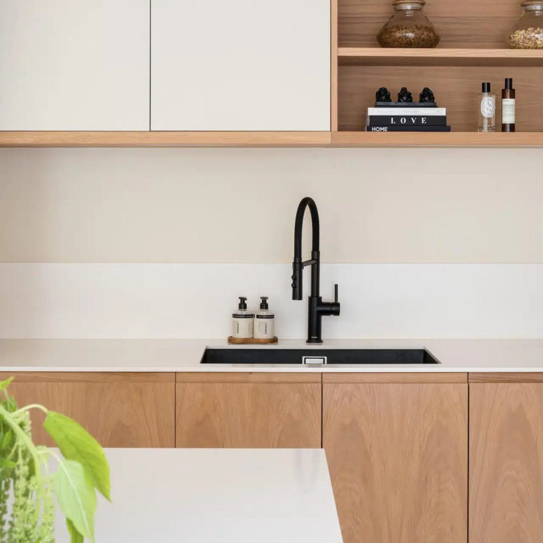 Clean white and oak kitchen cabinetry featuring integrated bespoke kitchen handle design, open shelving, and matte black tap by Sustainable Kitchens.