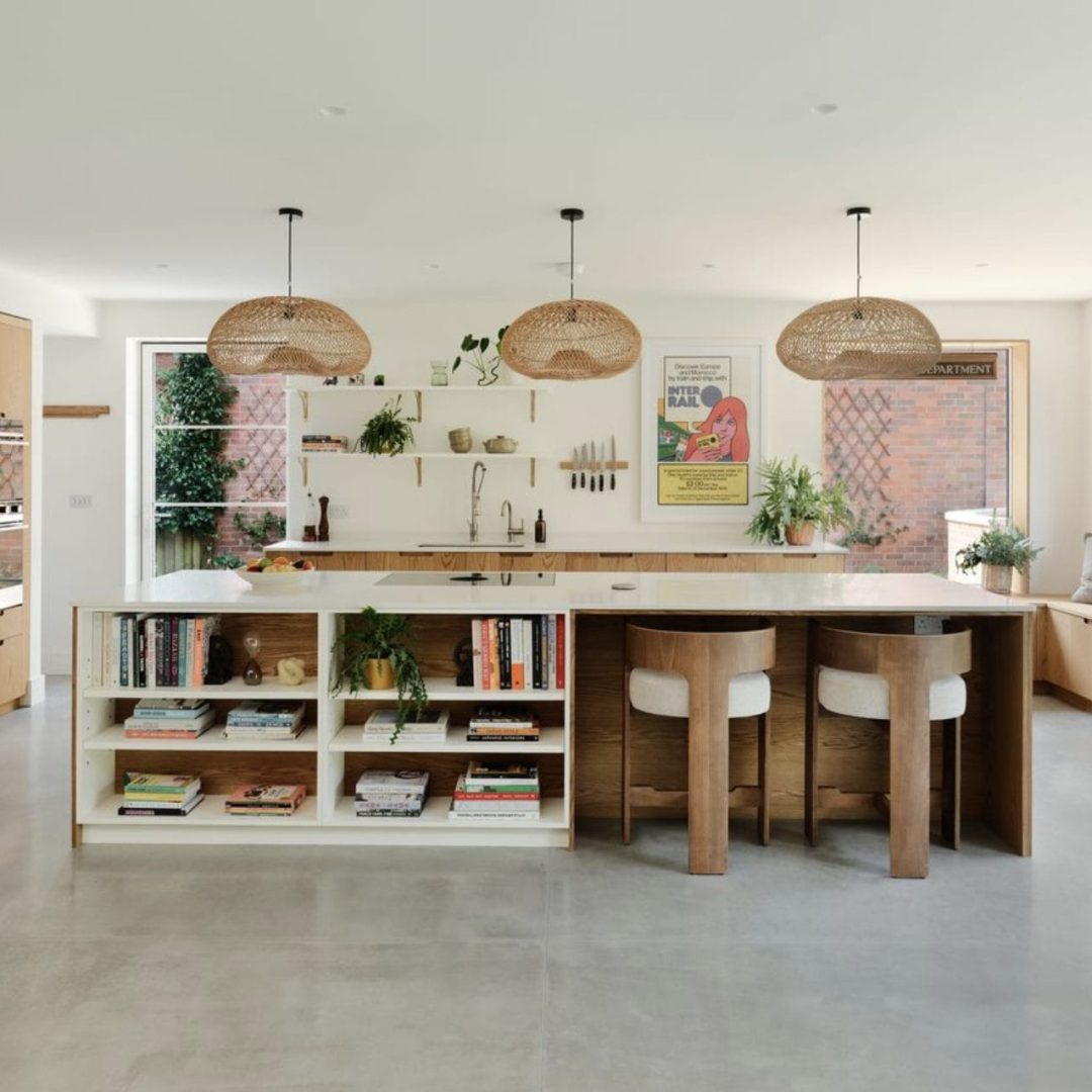 Large kitchen island with book storage, pendant lighting and oak cabinets with open shelving above.
